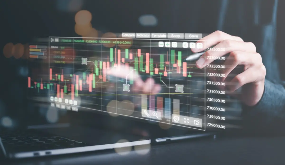 Person using a stylus on a transparent holographic financial stock trading chart over a laptop.