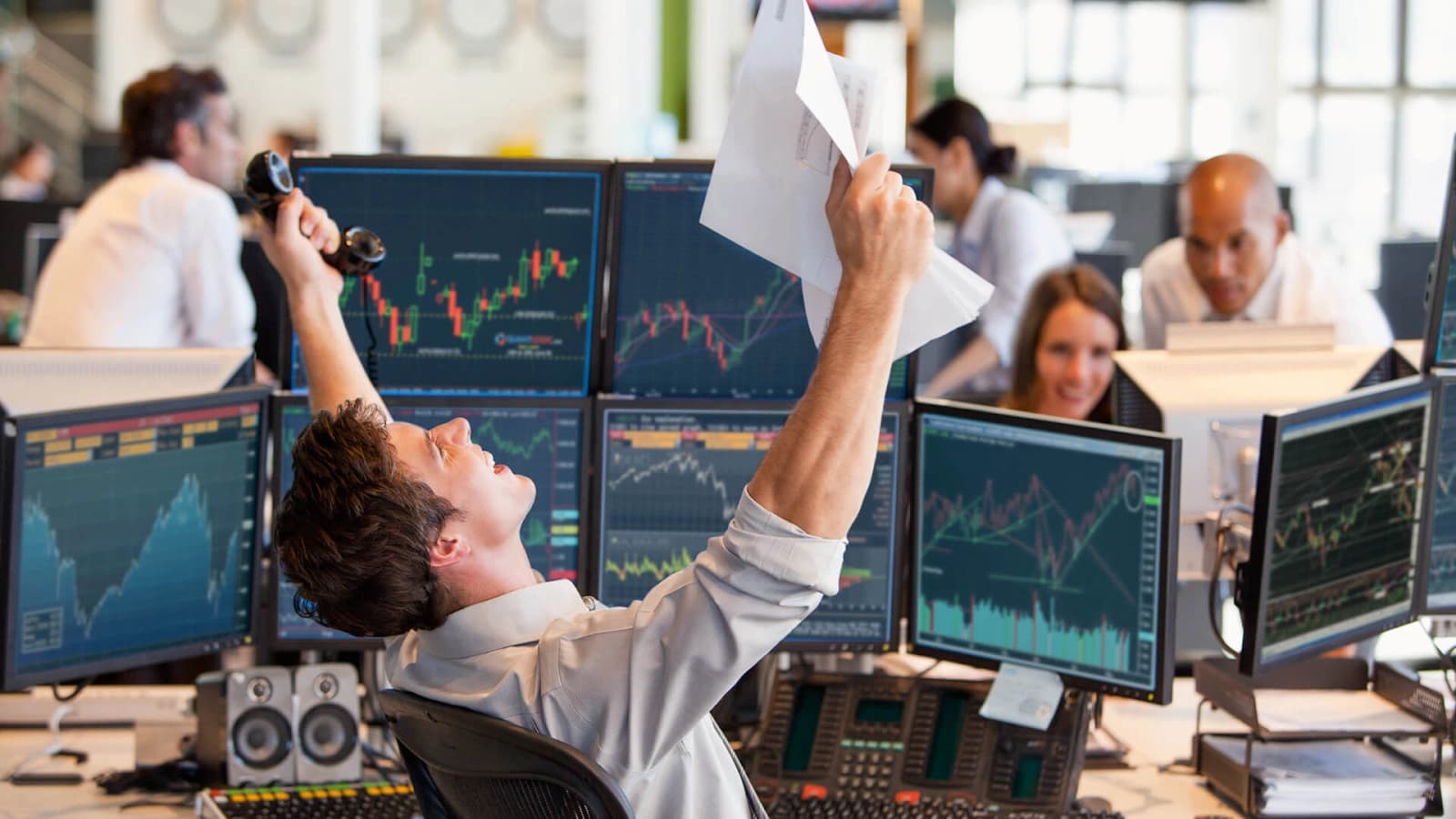 Trader celebrating in front of stock market screens.